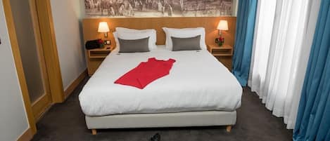 A neatly made bed with white linens and a red accent, two bedside lamps, a nightstand with a lamp, and a large framed picture above the bed.
