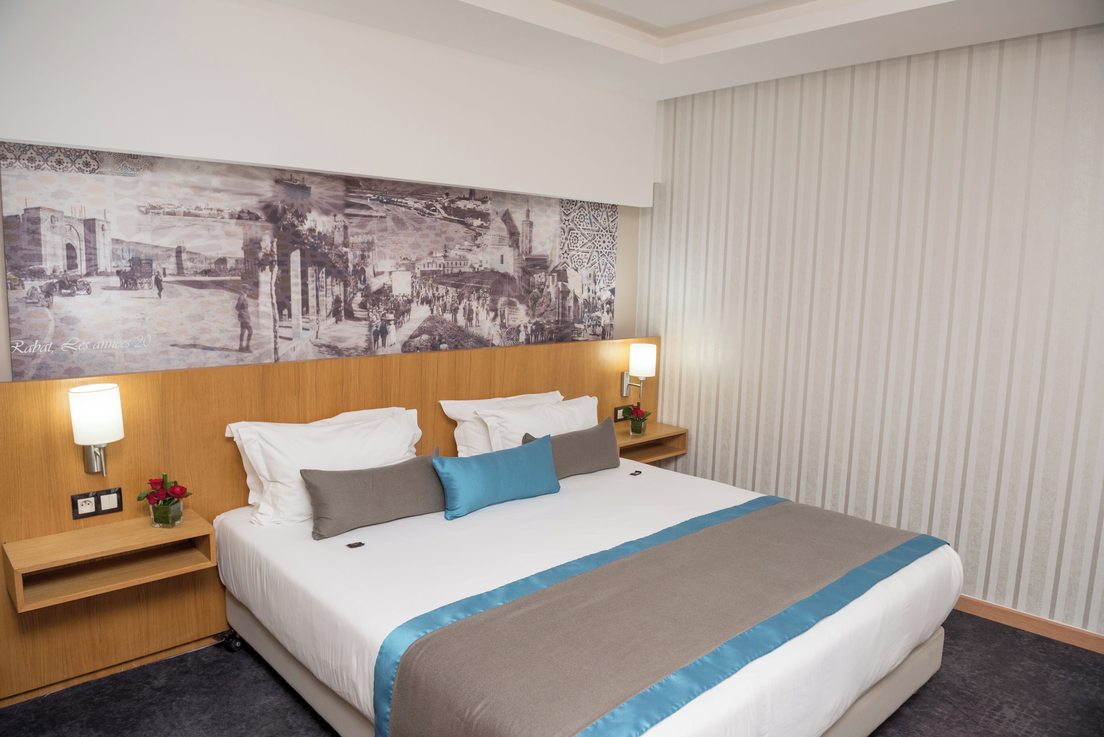A hotel room with a large bed, two bedside tables, a wall-mounted artwork, and a window with curtains.