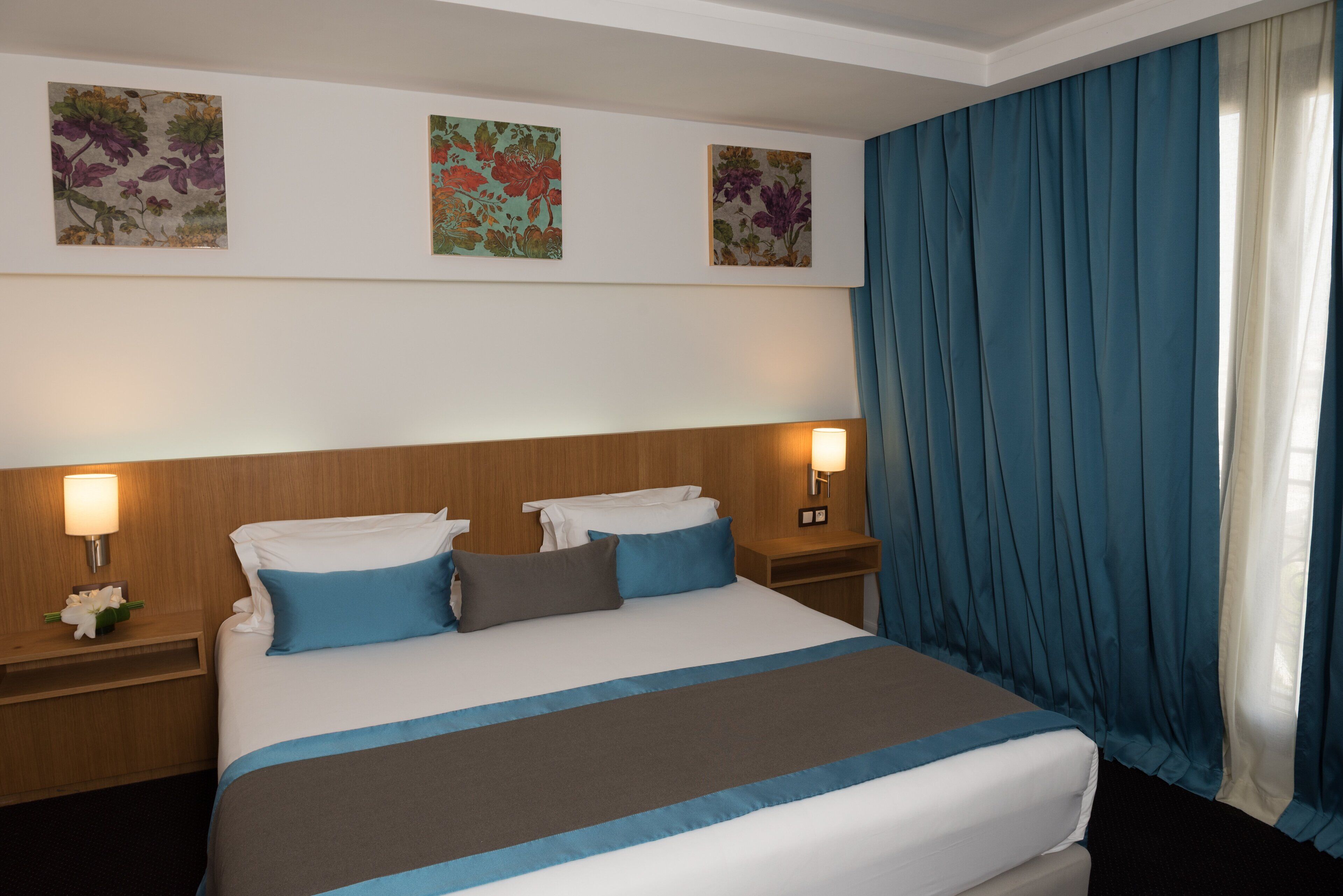 Una habitación de hotel con una cama grande, dos mesitas de noche y un ventanal con cortinas azules.