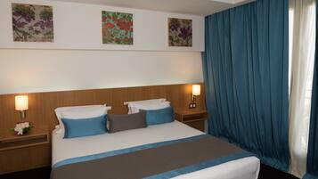 Una habitación de hotel con una cama grande, dos mesitas de noche y un ventanal con cortinas azules.