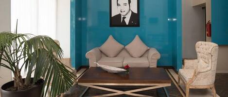 A room with a beige sofa, a coffee table, a potted plant, and a framed portrait on the wall.