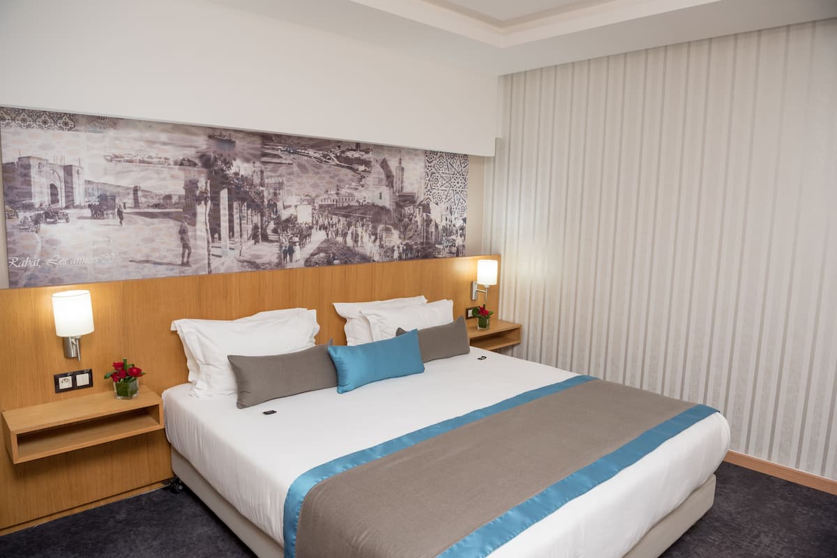 Ein Hotelzimmer mit einem großen Bett, zwei Nachttischen, einer Stehlampe und einem großen Stadtbild.