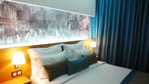 Habitación de hotel con una cama grande, dos lámparas de noche, una mesita de noche y un ventanal con vistas a un edificio histórico.