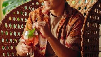 A person seated on a wicker chair with a drink in hand, surrounded by greenery.