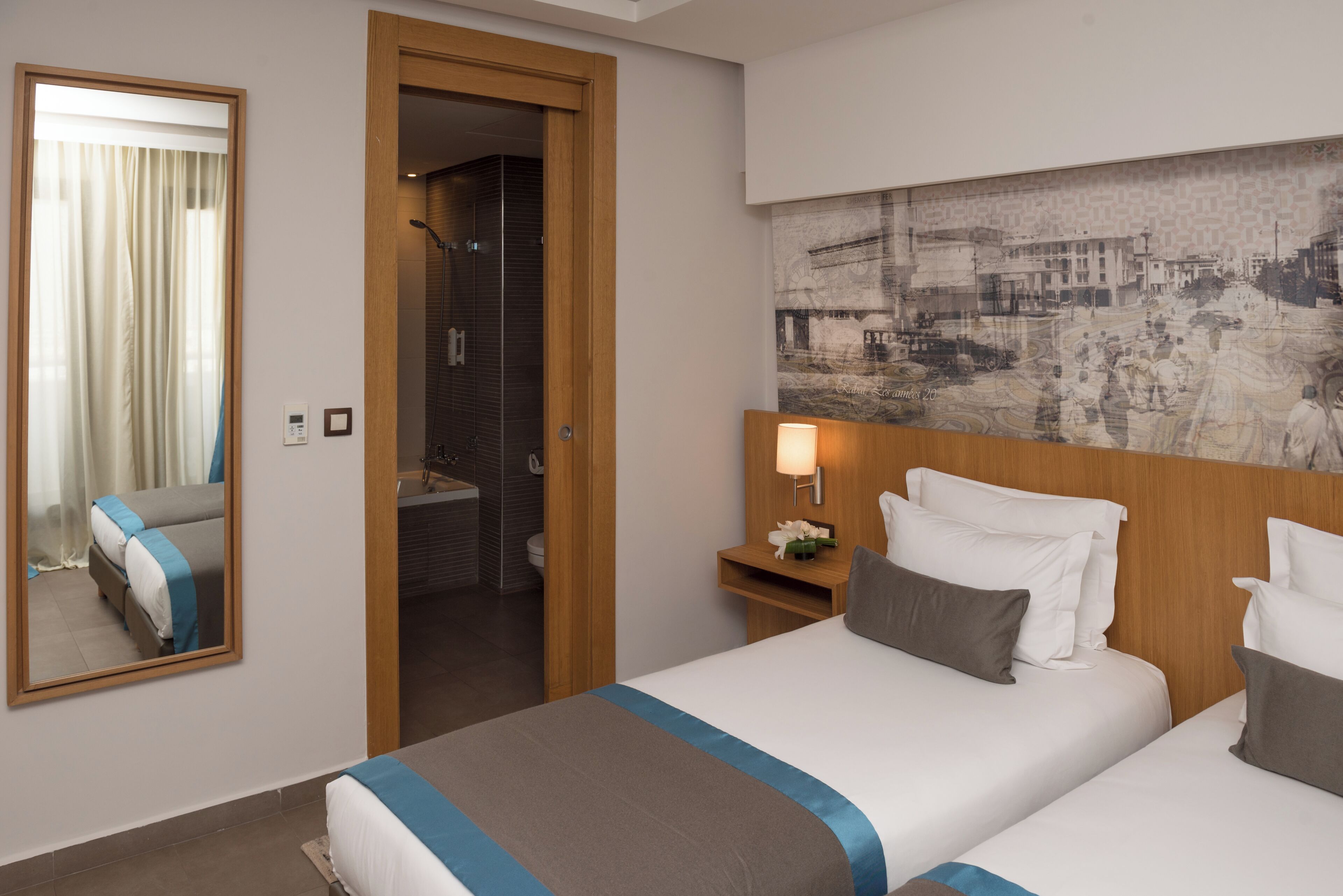 A hotel room with a bed, a mirror, a shower, and a wall-mounted artwork.