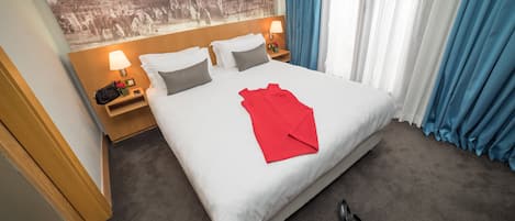 Une chambre d’hôtel avec un grand lit, une table de chevet avec une lampe, une serviette rouge et une paire de chaussures posées sur le sol.