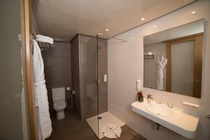 Un baño moderno con ducha de vidrio, lavamanos blanco y un espejo grande.