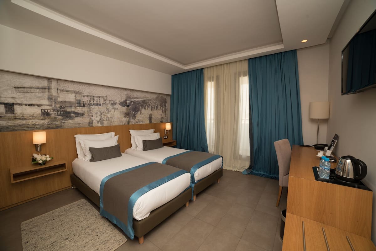 Ein Hotelzimmer mit zwei Betten, einem Schreibtisch, einem Stuhl, einem Fernseher und einem großen Gemälde an der Wand.