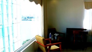 A room with a large window, a wooden chair, a small table with bottles, and a TV. - Paradise Hotel (Da Nang)