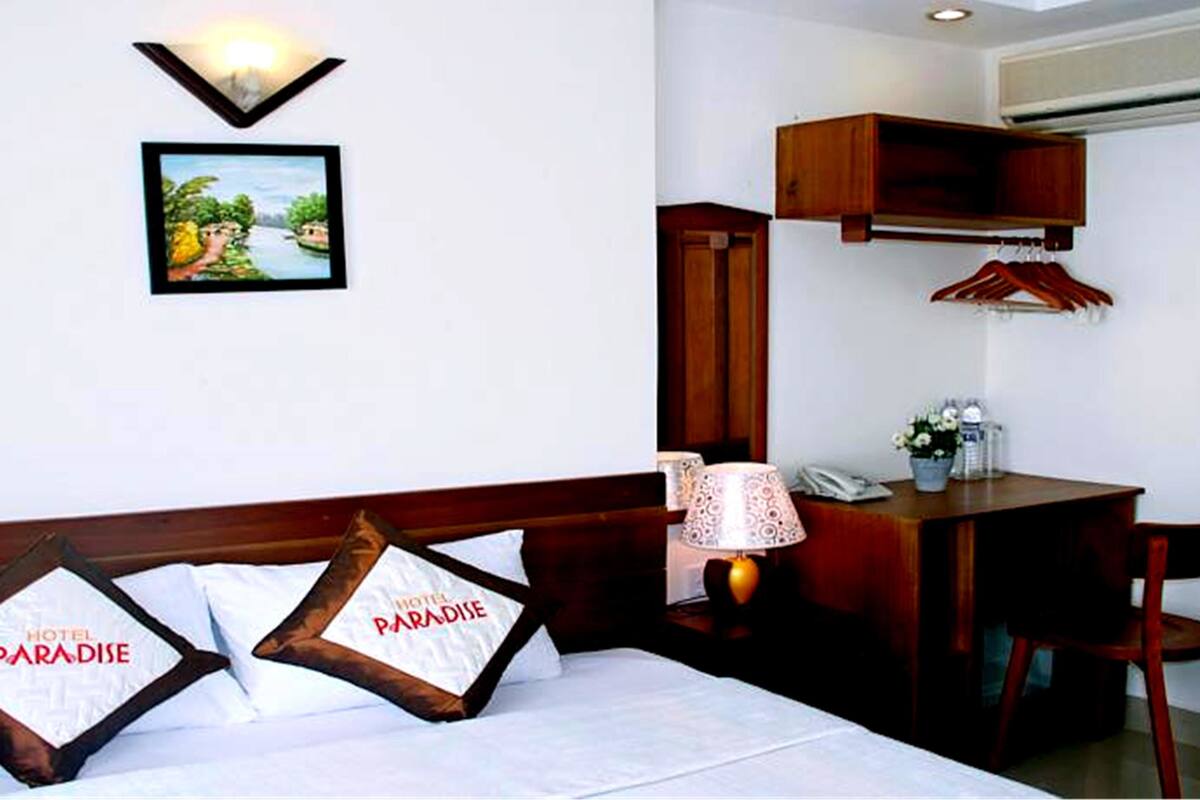 A hotel room with a bed, pillows, a desk, a lamp, and a picture on the wall.