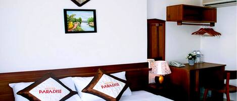 A hotel room with a bed, pillows, a desk, a lamp, and a picture on the wall.