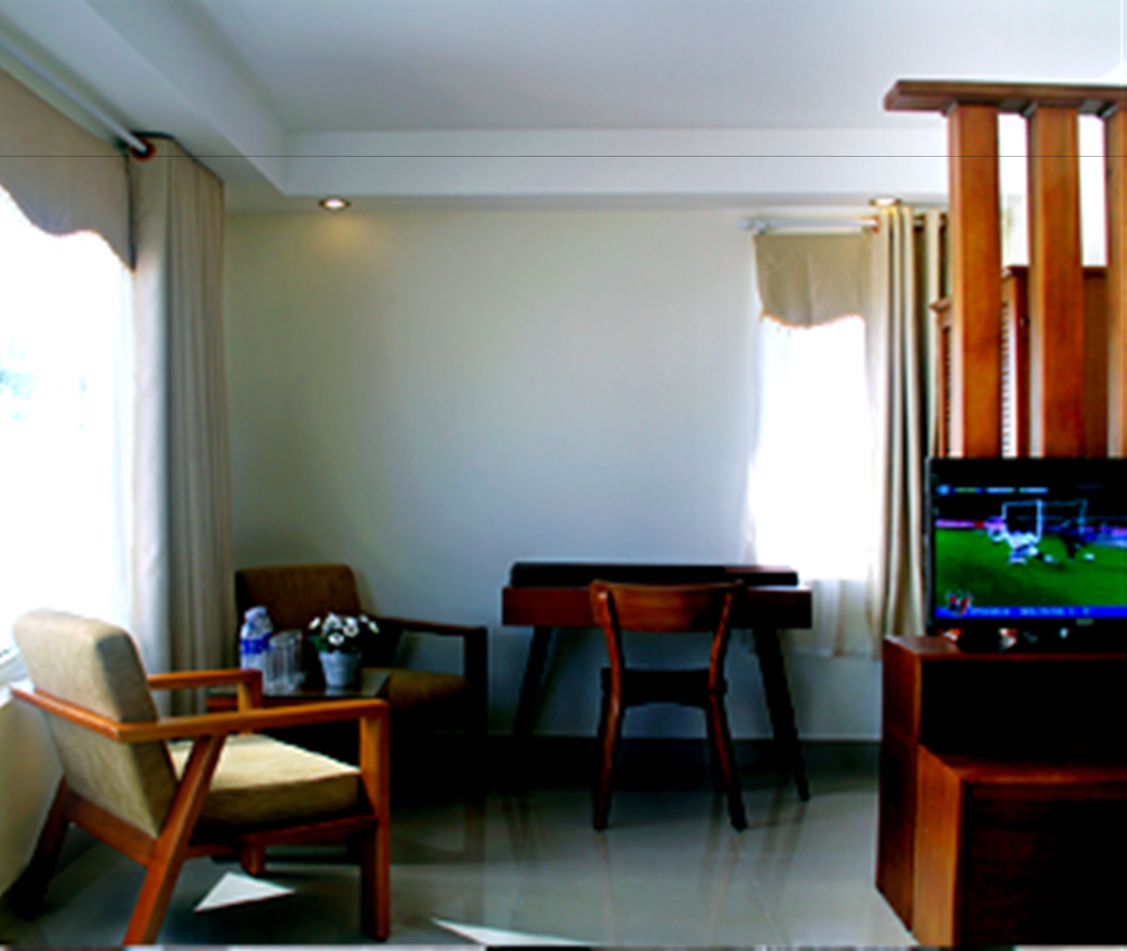 A hotel room with a wooden desk, two chairs, a television, and a window with curtains.