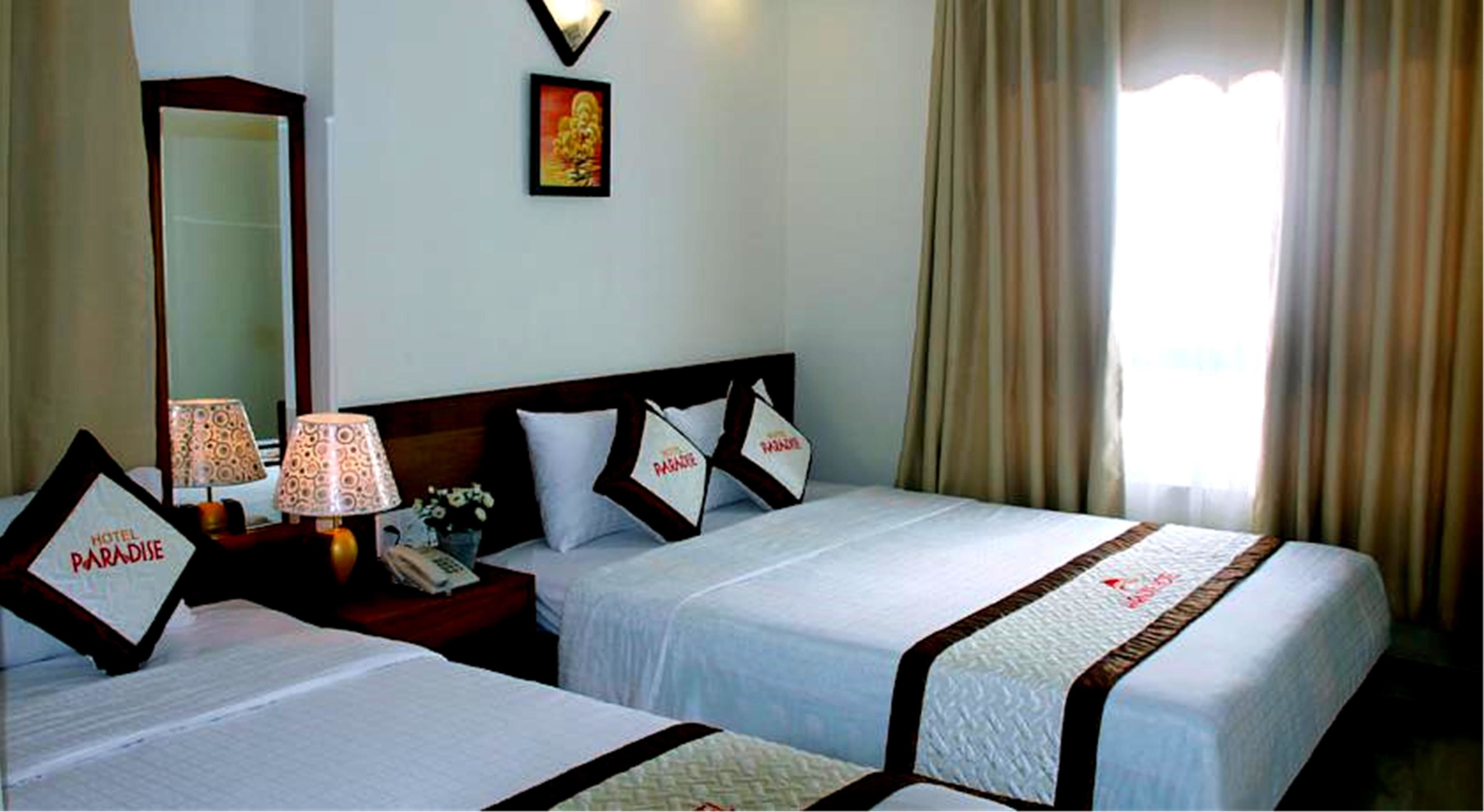 A hotel room with two beds, a nightstand with lamps, a mirror, and a window with curtains.