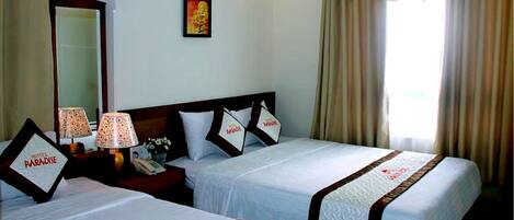A hotel room with two beds, a nightstand with lamps, a mirror, and a window with curtains.