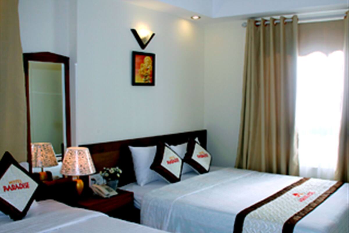 A hotel room with two beds, a nightstand with a lamp, a mirror, and a window with curtains.
