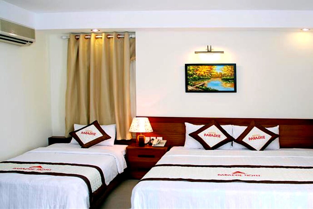 A hotel room with two beds, a nightstand with a lamp, a painting on the wall, and curtains.
