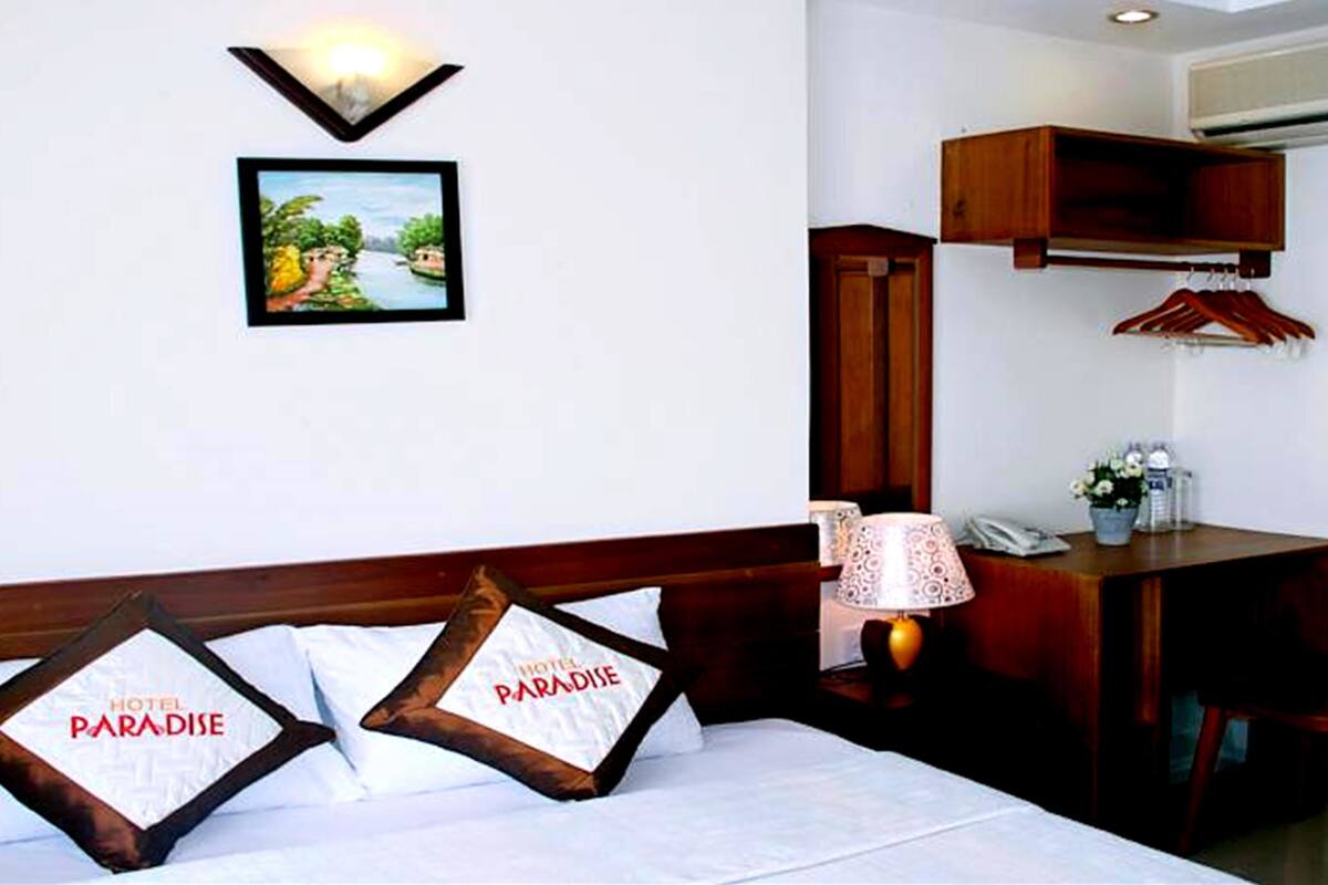 A hotel room with a bed, pillows, a desk, a chair, a lamp, a picture on the wall, and a wardrobe.