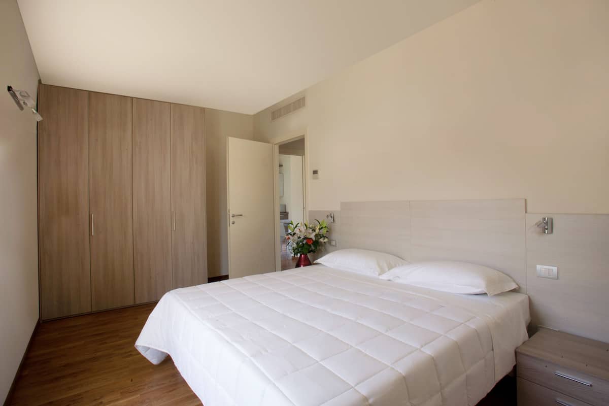 A bedroom with a large bed, wooden wardrobe, and a nightstand with a vase of flowers.