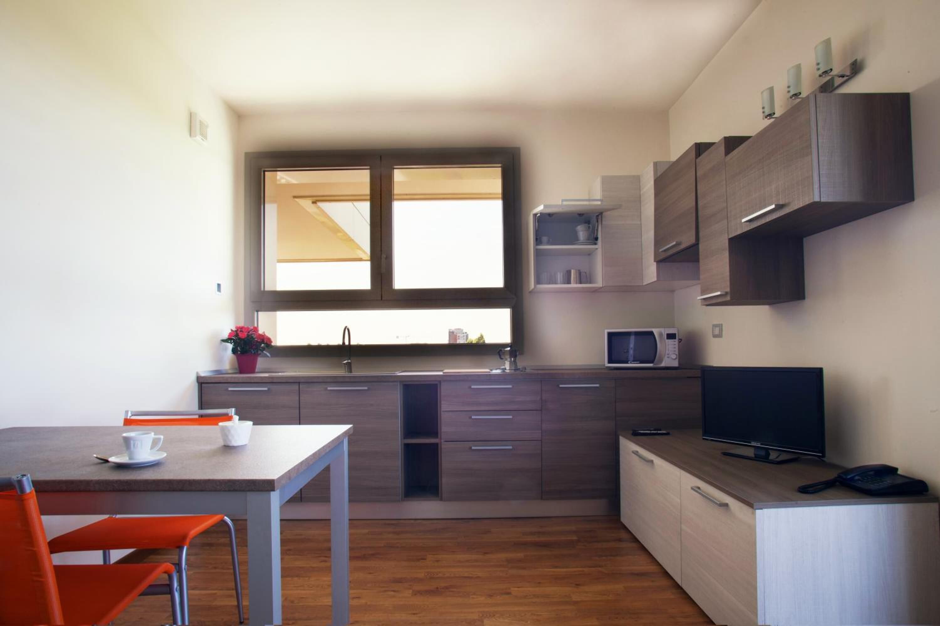 A compact kitchen with a dining area, a microwave, a TV, and a window providing natural light.