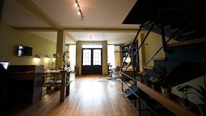 A spacious room with wooden flooring, a desk with a computer, a chair, and a bookshelf. There is a staircase with a railing and a door leading to another room. - Hotel 27 (Tbilisi)