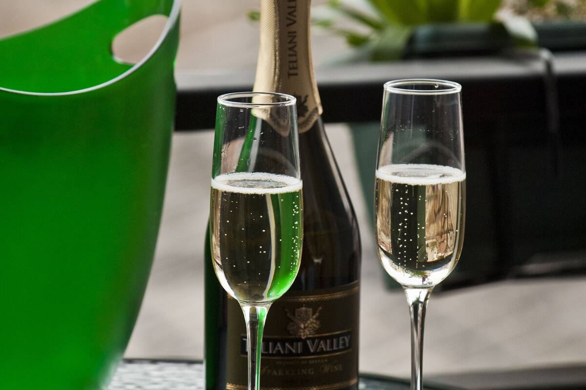 A bottle of wine and two glasses on a table with a green bowl and a plant in the background.