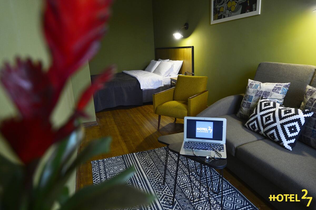 A hotel room with a bed, a sofa, a laptop on a small table, and a patterned rug.