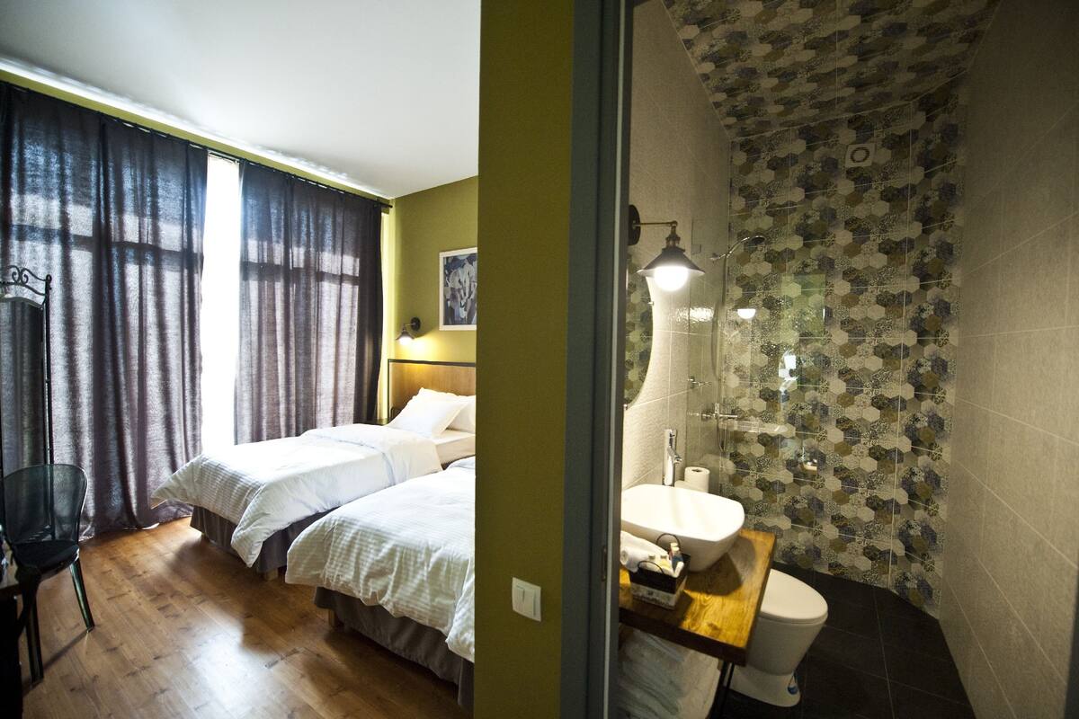 A room with two beds, a chair, a sink, and a shower with patterned tiles.