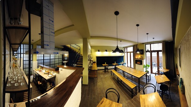 A restaurant with a long counter, multiple seating areas, and a staircase leading to an upper level. - Hotel 27 (Tbilisi)