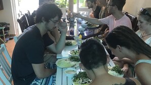 Un grupo de personas cenando en una mesa con sillas blancas, un separador de vidrio y vistas al exterior.