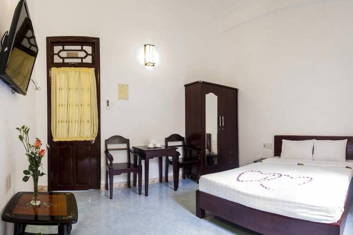 A hotel room with a bed, a desk, a chair, a wardrobe, and a wall-mounted TV.