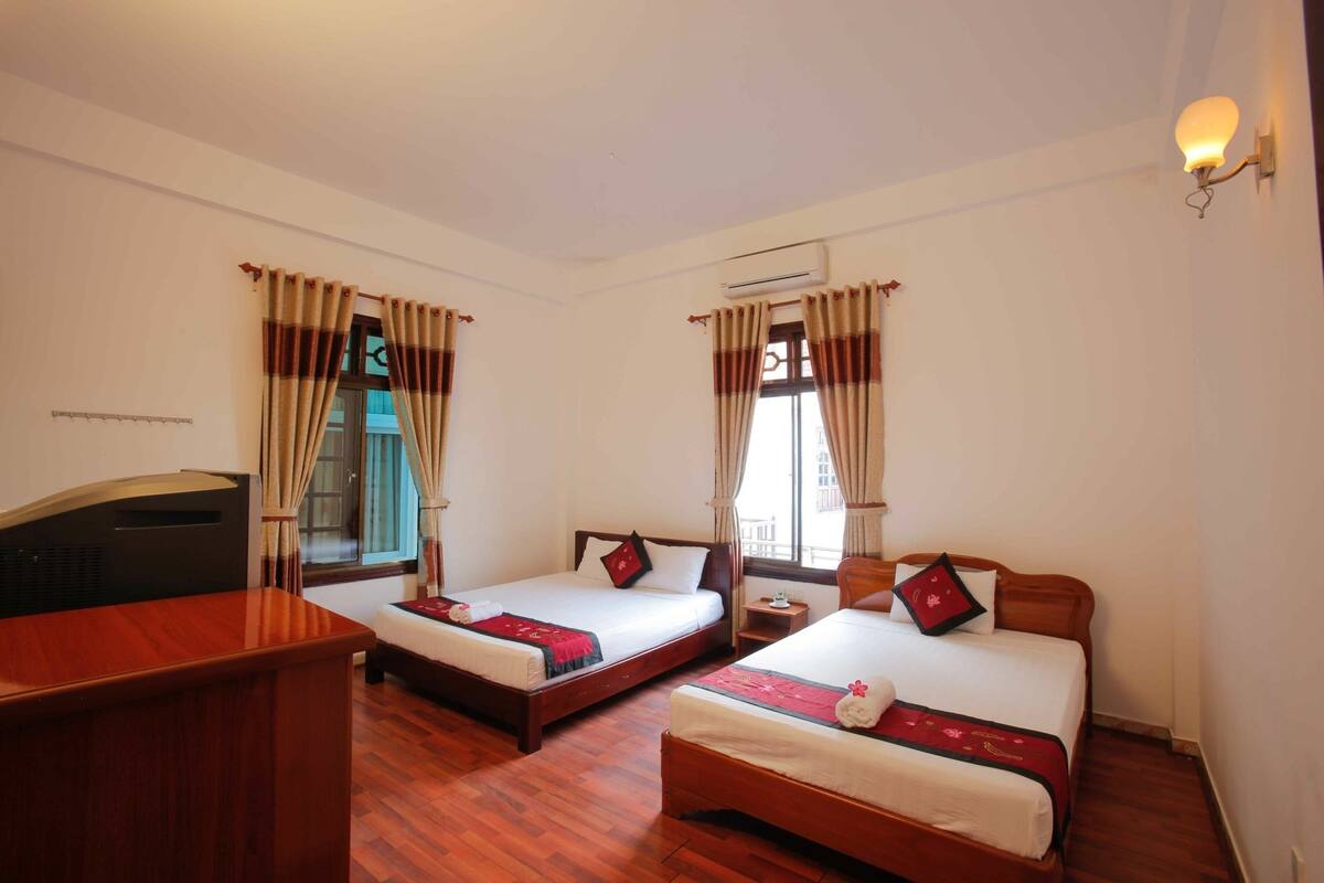 A hotel room with two single beds, a desk, and a window with curtains.