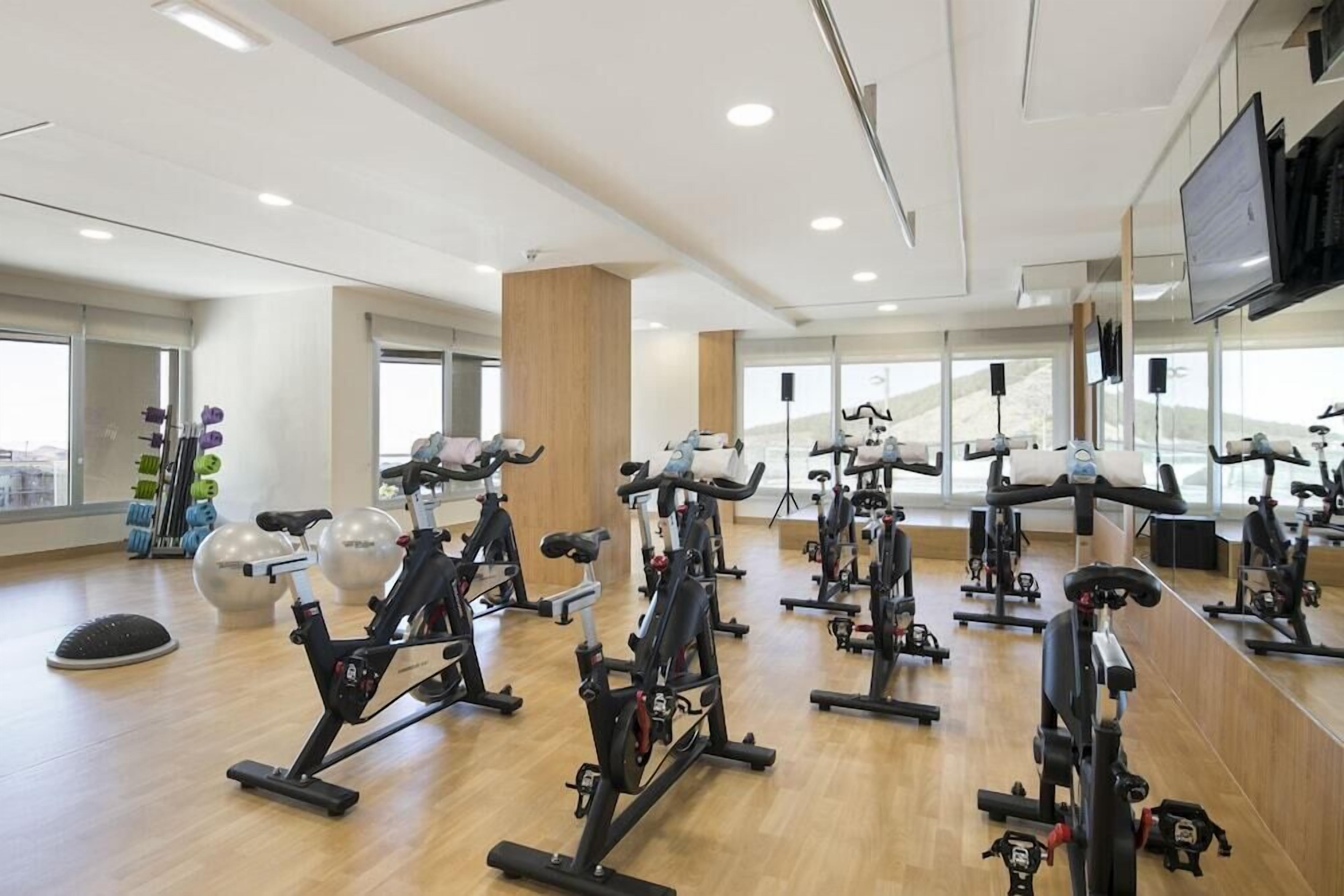 A gym with multiple stationary bikes, large windows, and a wooden floor.