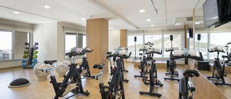 A gym with multiple stationary bikes, large windows, and a wooden floor.