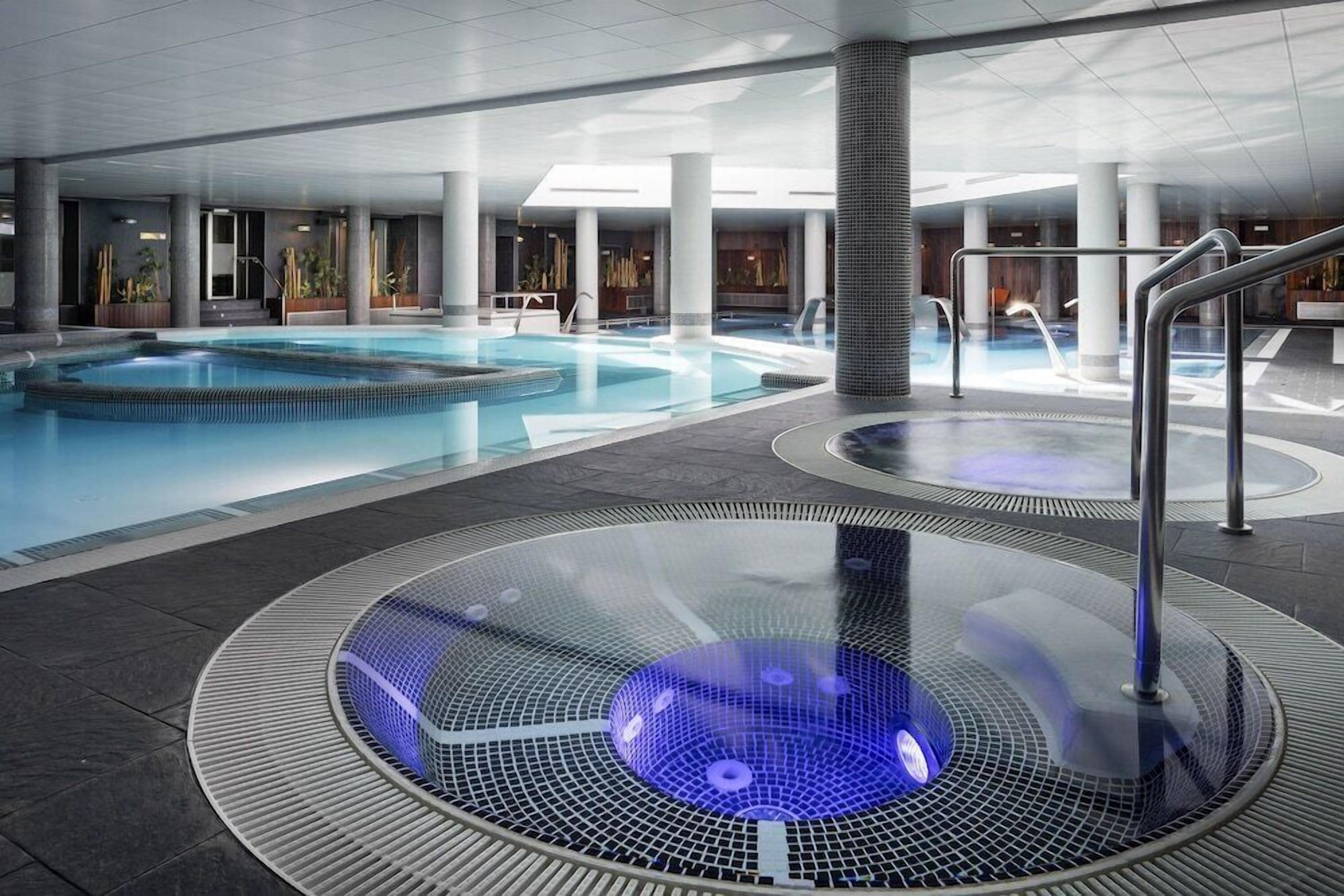 A modern indoor pool area with a hot tub and a separate swimming pool.