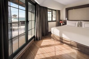 Habitación de hotel con una cama grande, vista al mar a través de un ventanal corredero y un balcón.
