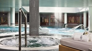 Un área de spa con hidromasaje, una tumbona y una piscina con chorros de agua.