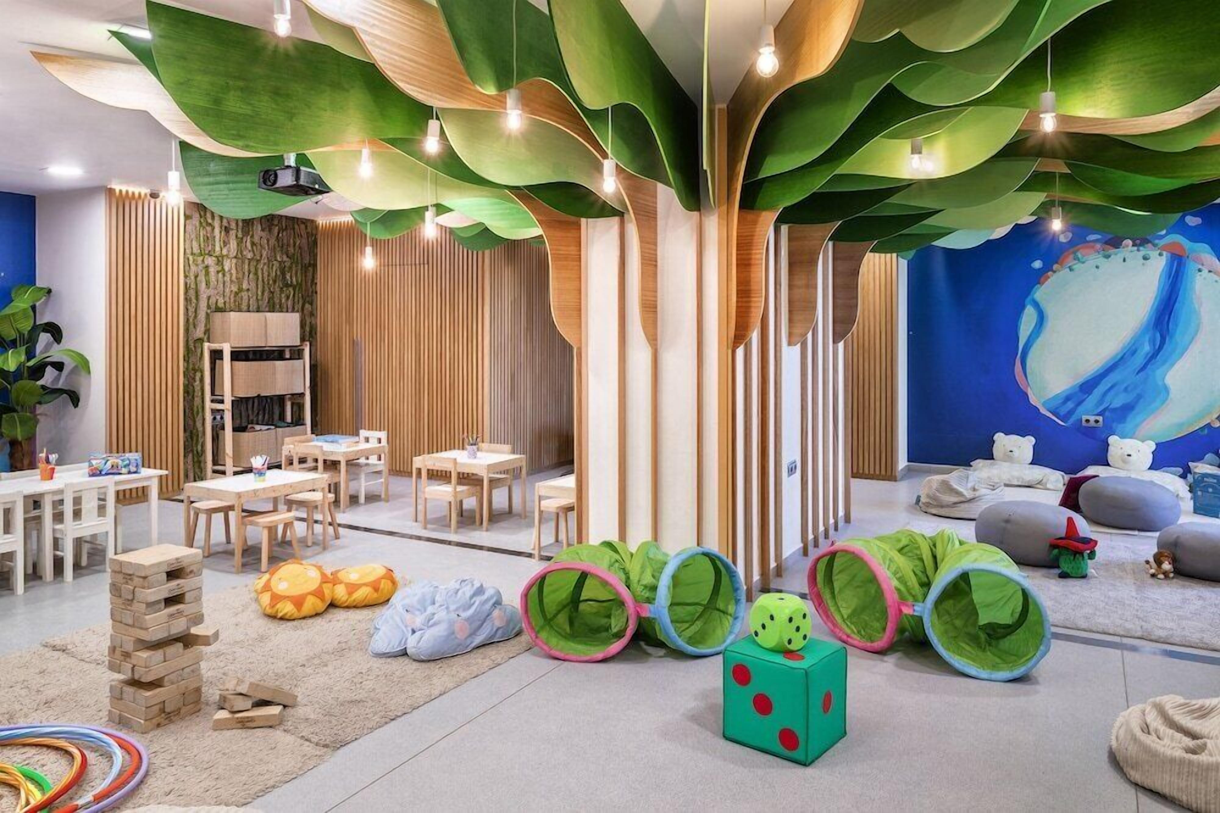 A children's play area with a large tree structure, play tents, and a mural on the wall.