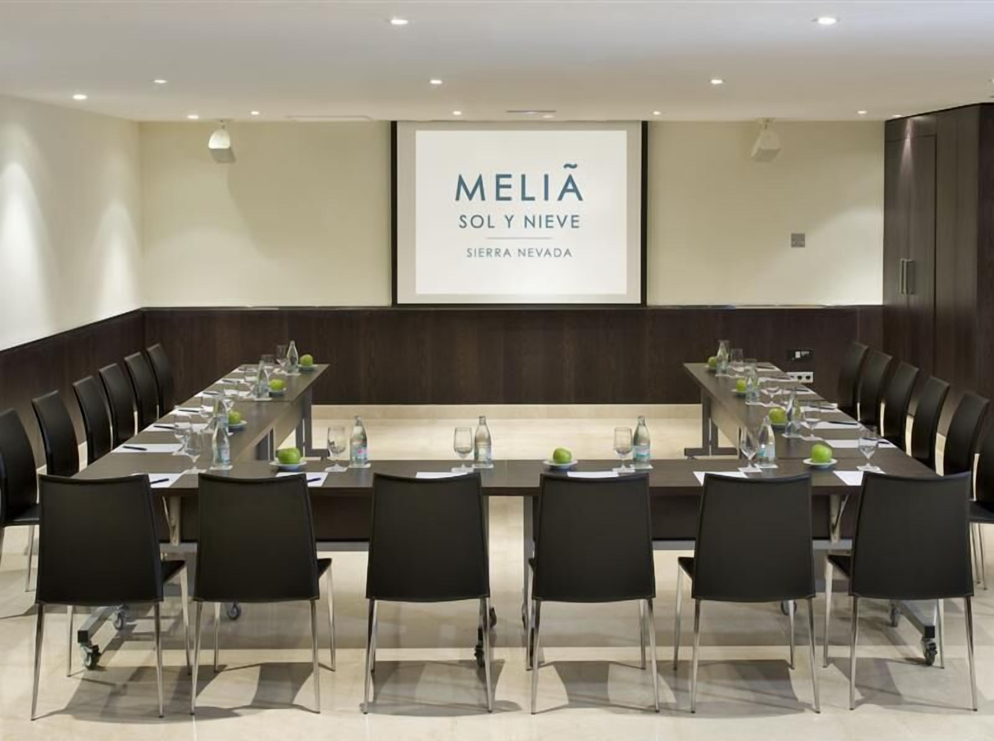 Une salle de conférence avec une longue table, des chaises noires et un grand écran affichant le texte « MELIA SOL Y NIEVE SIERRA NEVADA ».