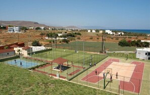 Een sportterrein met verschillende basketbal- en tennisbanen, omringd door woongebouwen en een bergachtig landschap.