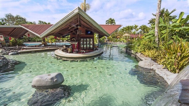 A tropical resort with a clear pool, a bar area, and lush greenery. - Arenal Springs Resort (La Fortuna)