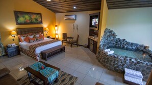 A hotel room with a bed, a small dining area, a stone hot tub, and a TV. - Arenal Springs Resort (La Fortuna)