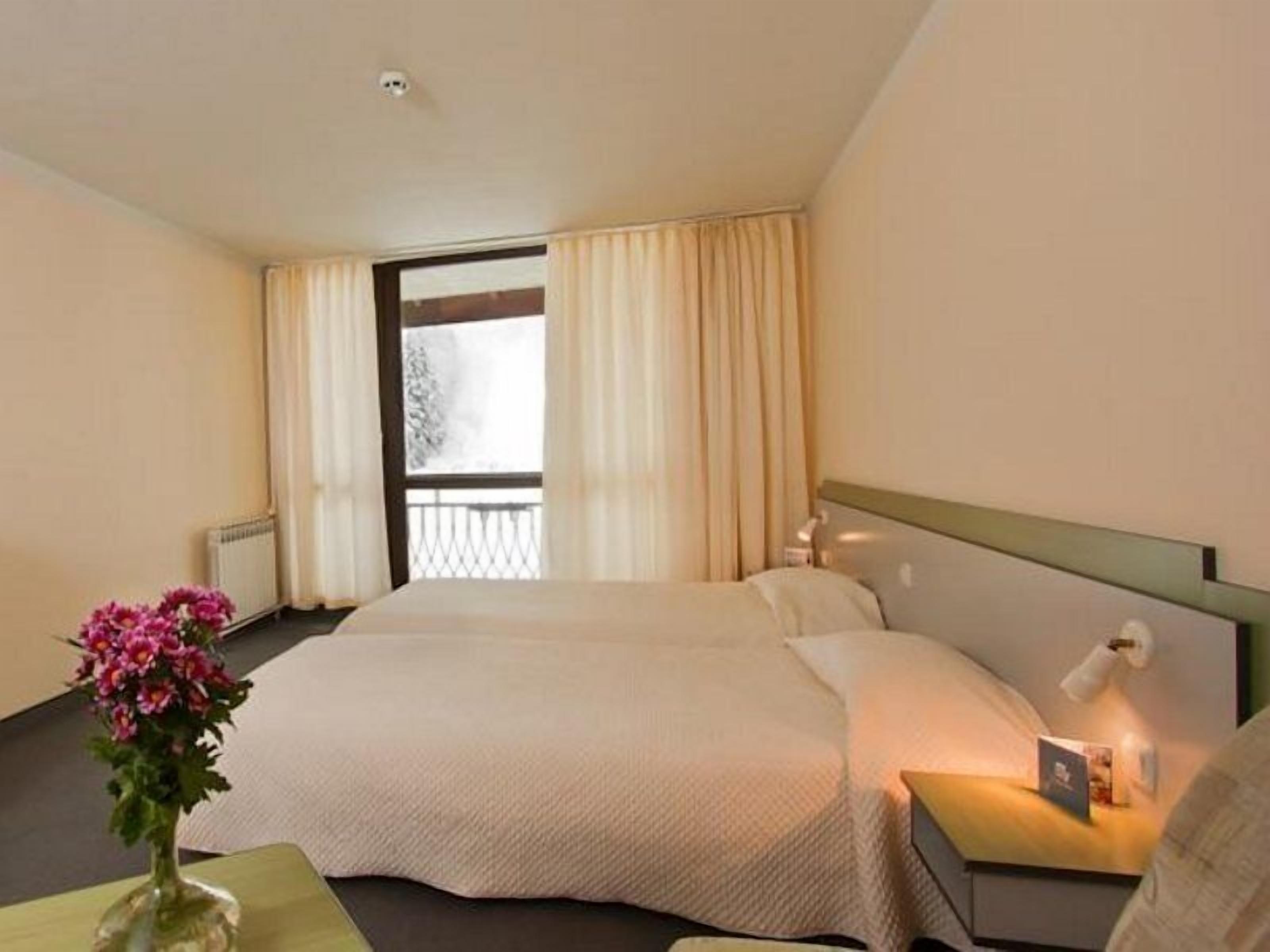 A hotel room with a large bed, a bedside table with a lamp, and a window with curtains.