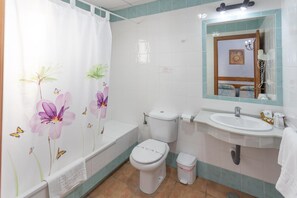 Une salle de bain équipée de toilettes, d’un lavabo et d’un rideau de douche orné de motifs floraux.