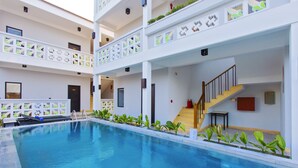 Una piscina coperta a più livelli con acqua cristallina, circondata da pareti bianche con motivi geometrici, e una scala che conduce a un livello superiore.