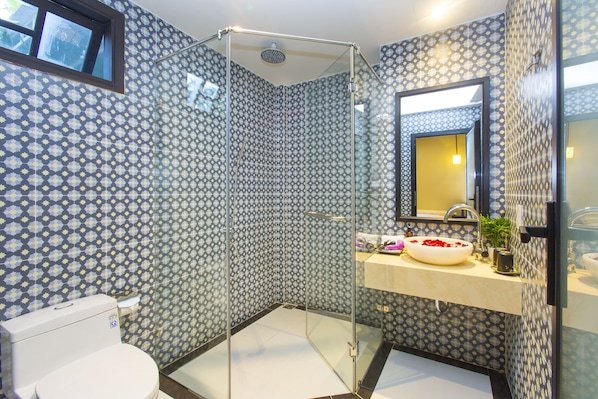 Un baño con paredes estampadas, ducha con cerramiento de vidrio, lavamanos blanco y espejo sobre él.