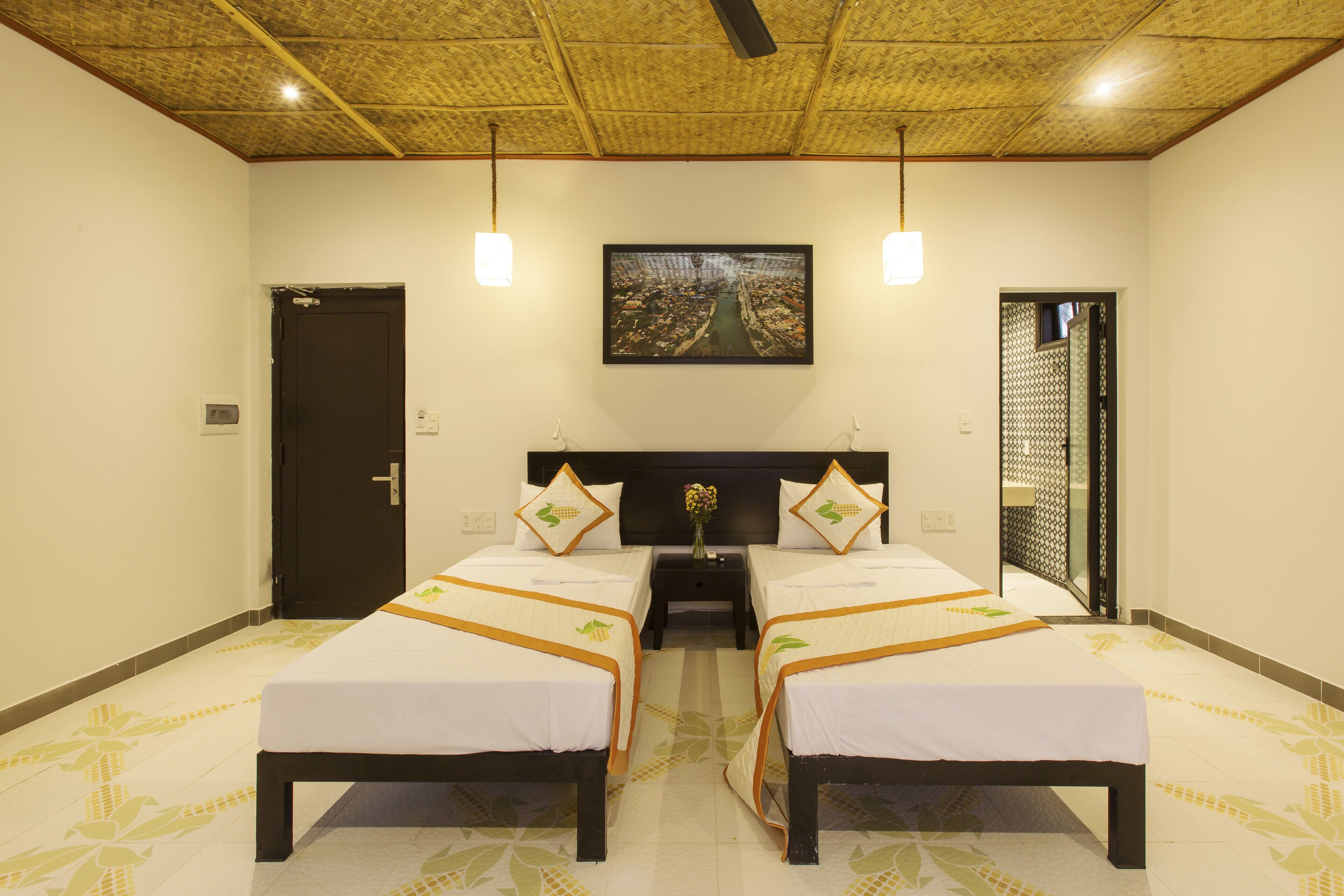 A hotel room with two beds, a wooden ceiling, a painting on the wall, and a door.
