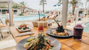 Una mesa de comedor con diversos platos y bebidas en un restaurante junto a la piscina.