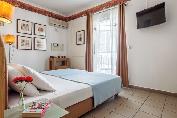 Une chambre d’hôtel avec un lit, une table de chevet sur laquelle se trouvent un livre et des fleurs, un téléviseur fixé au mur et une fenêtre avec des rideaux.