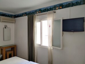 Habitación de hotel con cama, televisor montado en la pared, ventana con cortinas y aire acondicionado en la pared.