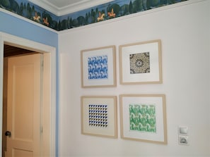 Une pièce dont les murs sont ornés de quatre œuvres d’art encadrées, avec une porte et une peinture murale au plafond.